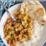 A plate with flavorful cauliflower curry, white rice, and naan bread, served with a spoon.