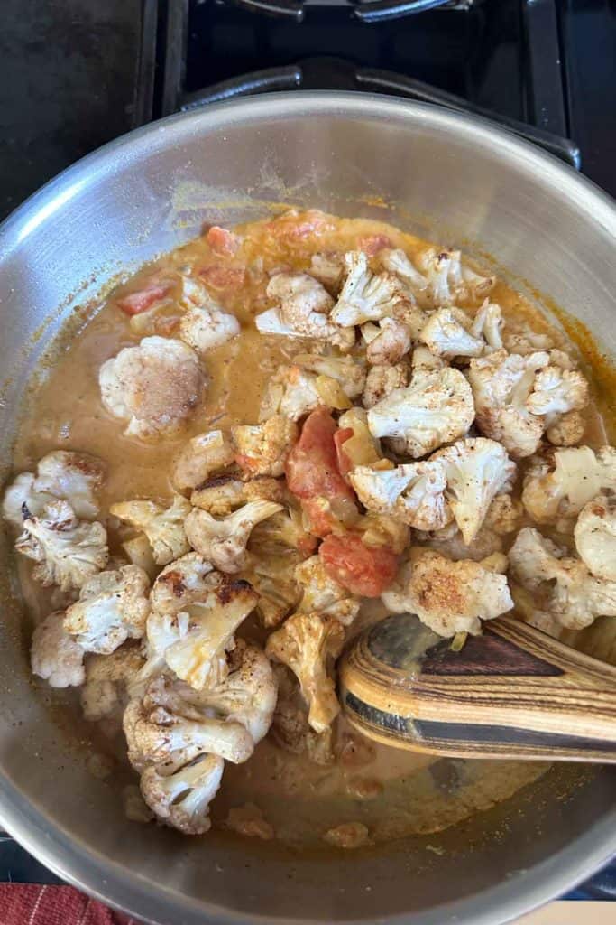 Cauliflower being added to curry sauce.