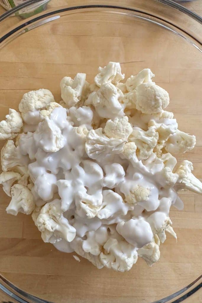 Cauliflower and coconut milk in a mixing bowl before mixing.