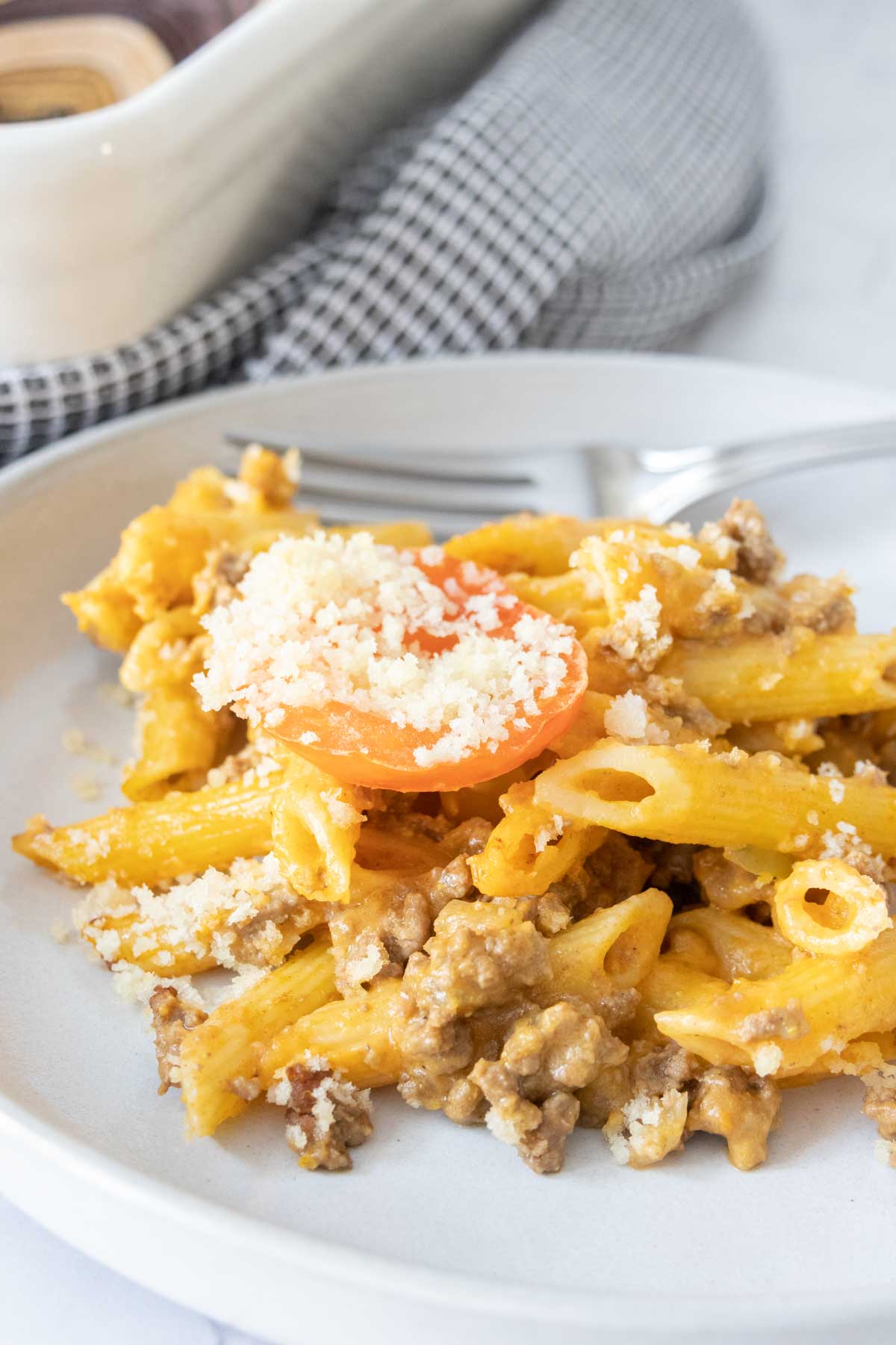 Plate of cheeseburger mac and cheese with breadcrumbs and tomato on top.