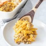 Wooden spoon serving cheeseburger mac and cheese onto plate.