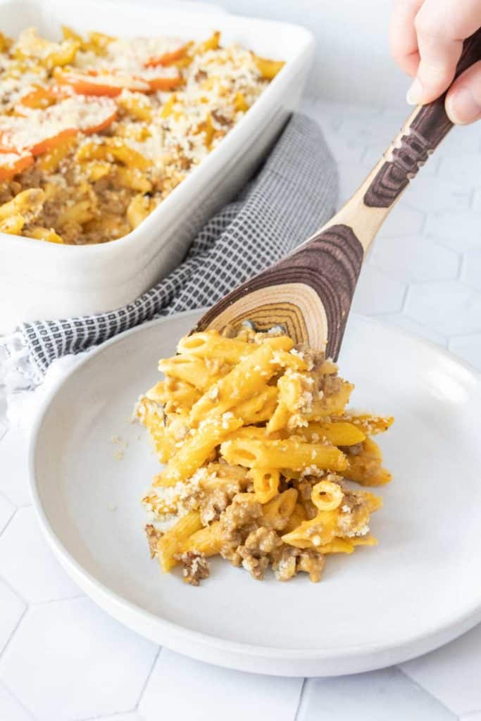 Wooden spoon serving cheeseburger mac and cheese onto plate.