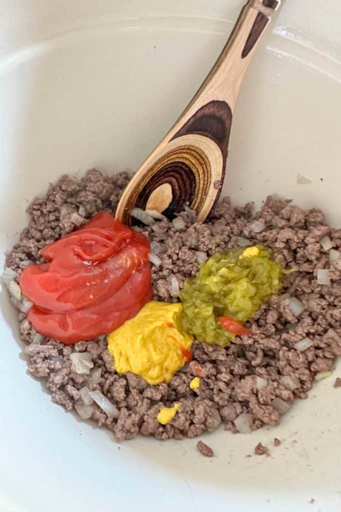 Mixing bowl with beef, onion, ketchup, mustard, and relish.