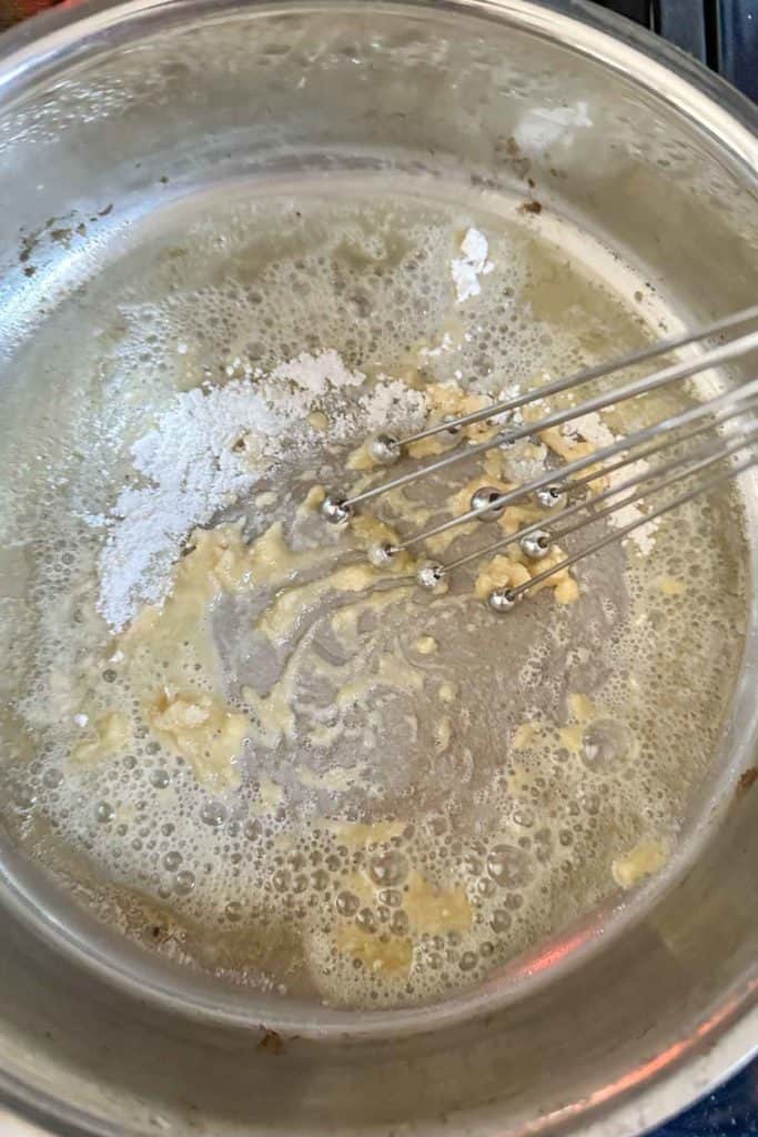 Whisking flour into melted butter to make roux.