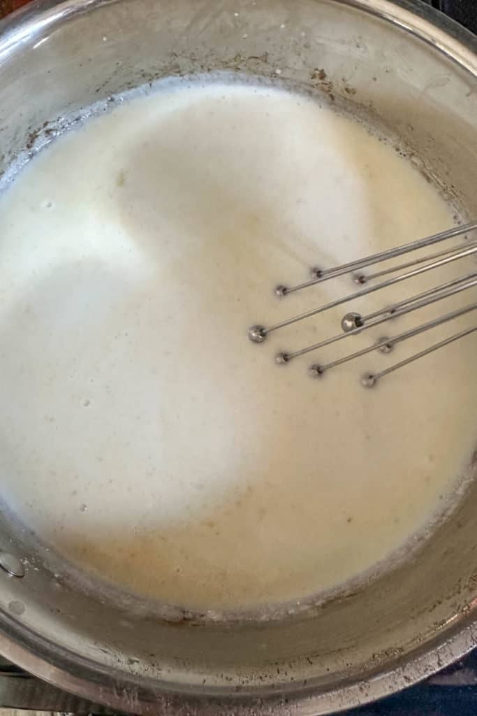 Cooking milk and roux to make cheese sauce.