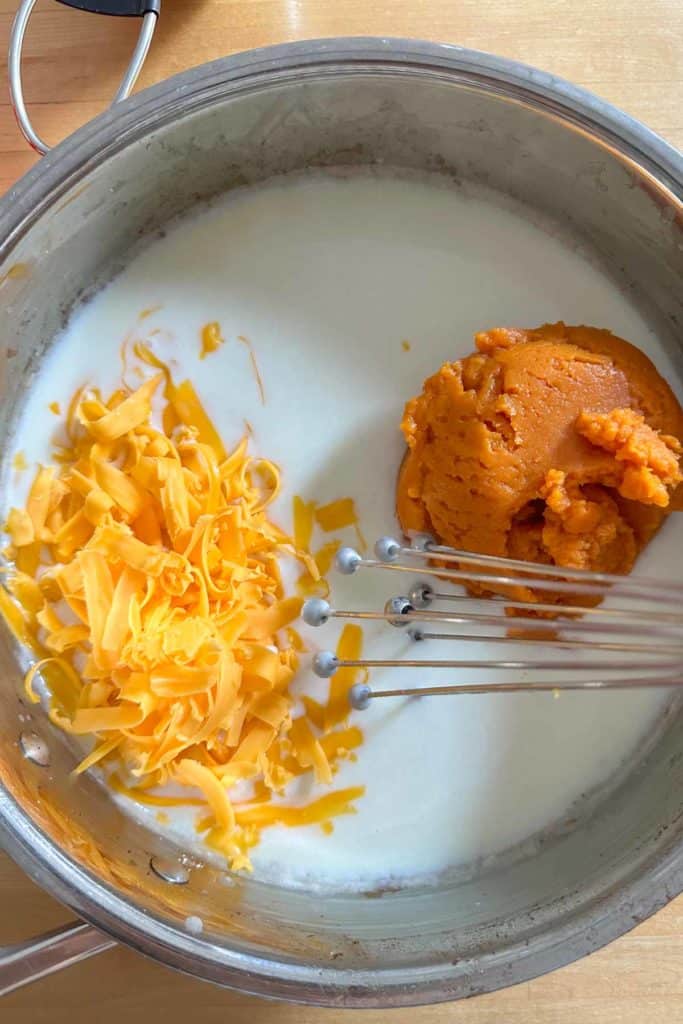 Cheese and pumpkin being added to milk mixture for cheese sauce.