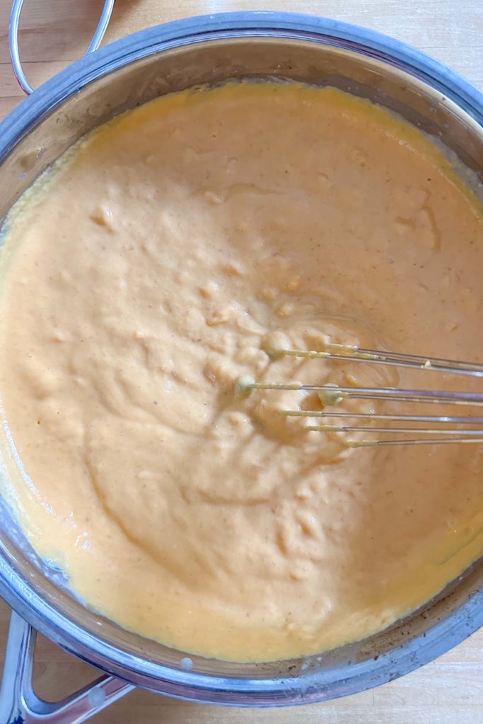 Whisking cheese sauce in a pan to make smooth.