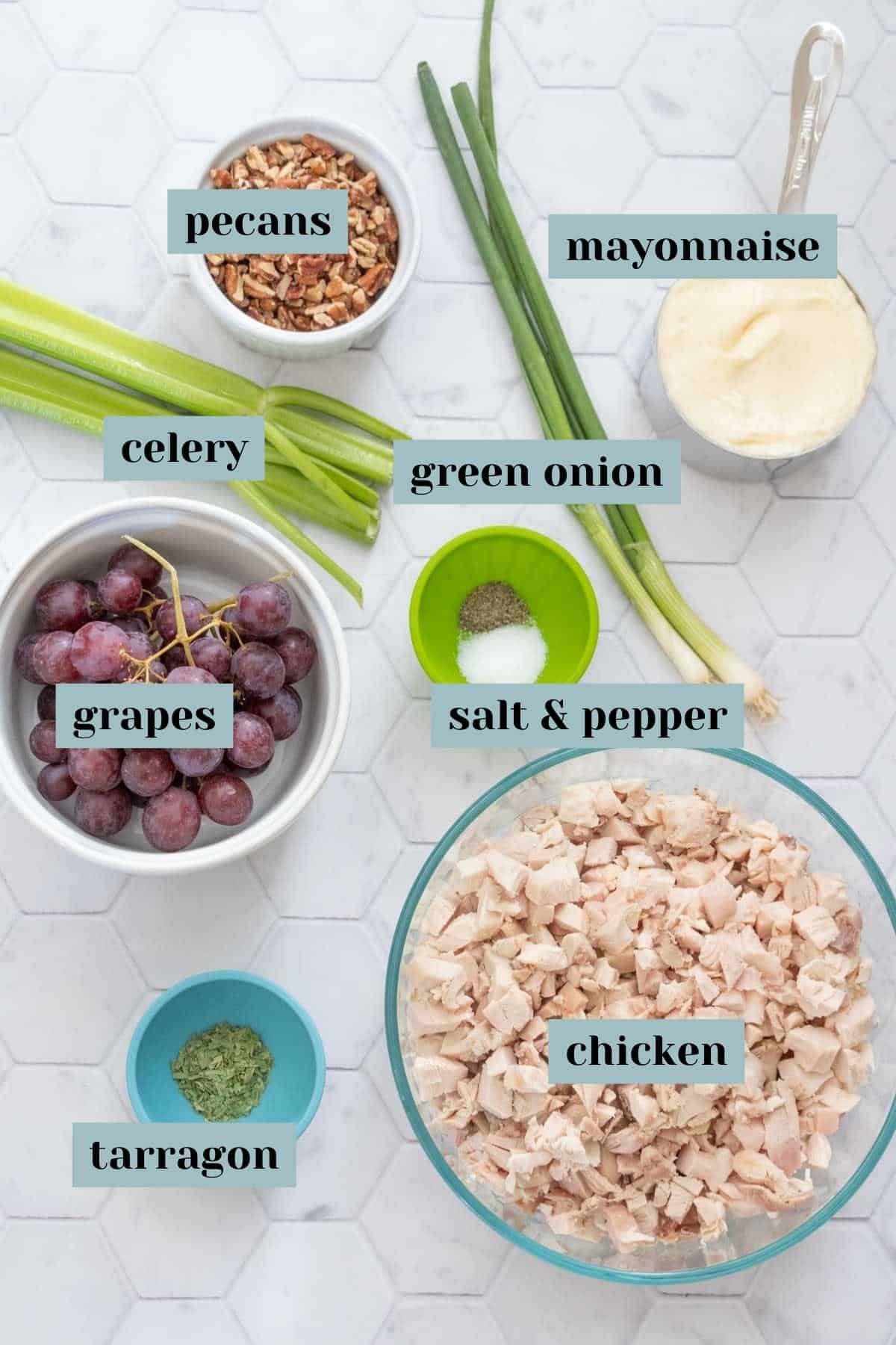 Ingredients for chicken salad on a tile surface with labels.