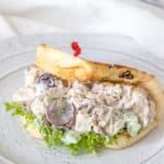 Chicken salad with grapes in a folded over flatbread on a gray plate.