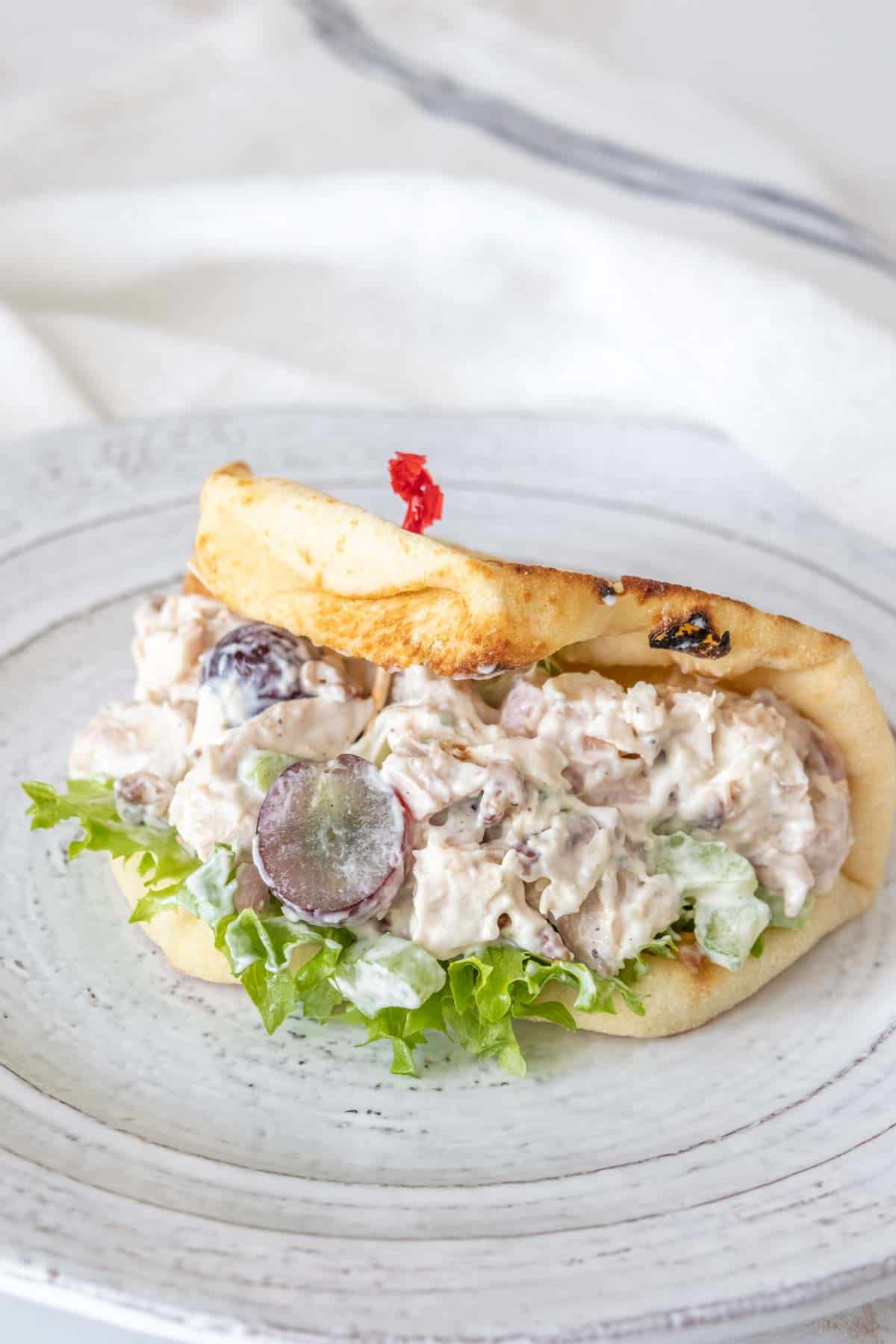 Chicken salad with grapes in a folded over flatbread on a gray plate.