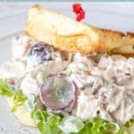 Chicken salad with grapes served on a bun with crisp lettuce, beautifully displayed on a plate.