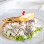 Chicken salad with grapes served in a pita bread on a white plate, garnished with lettuce and secured by a red toothpick.