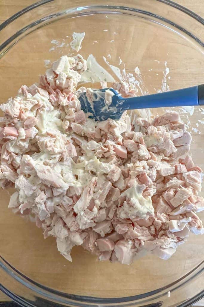 Mixing together diced chicken and mayonnaise in a glass bowl.