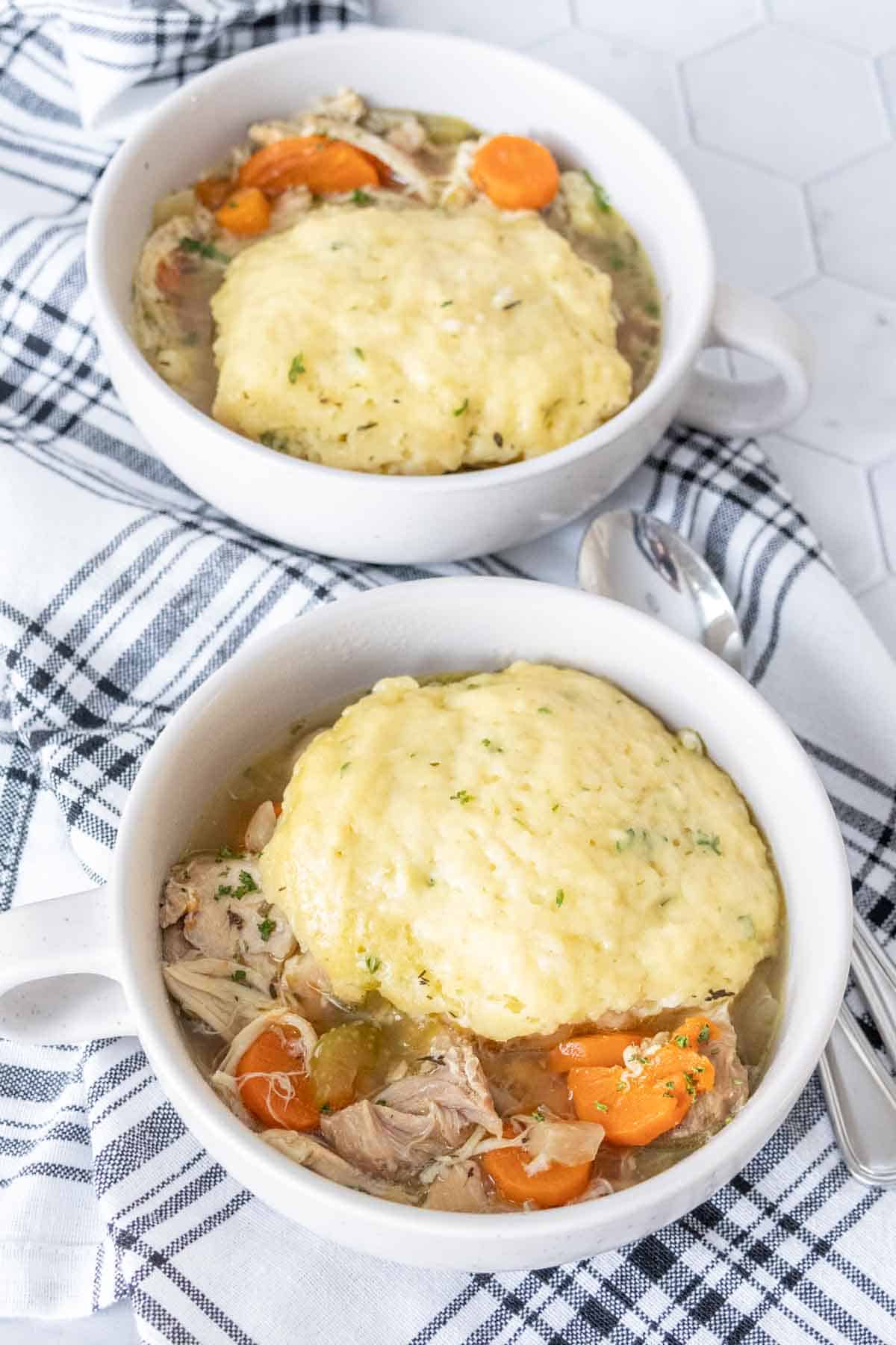 Two bowls filled with chicken and dumplings with spoons next to the bowls.