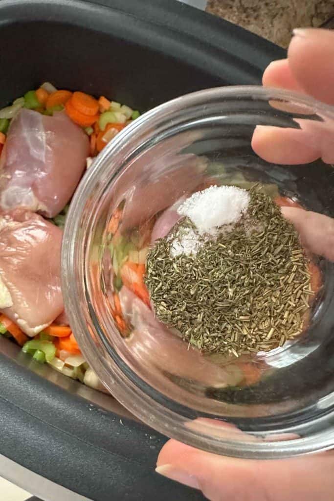 Herbs and spices for chicken and dumplings in a glass prep bowl being added to slow cooker.