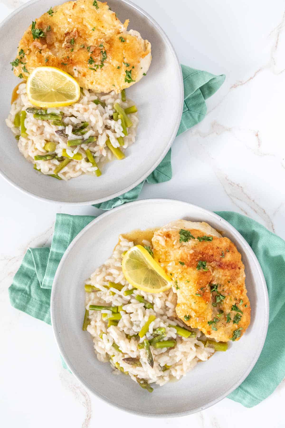 Overhead of lemon chicken and asparagus risotto on plates.