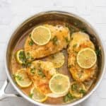 Skillet with cooked chicken breasts, lemon, and parsley.