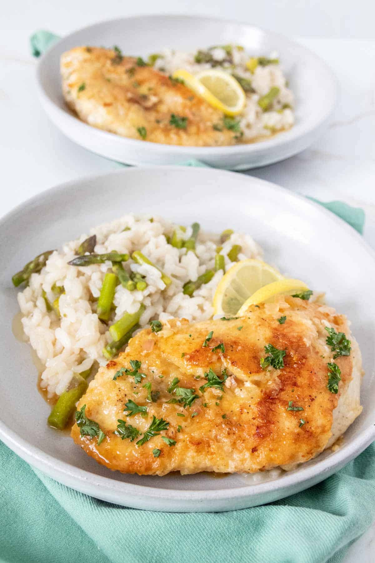 Two plates of lemon chicken breast with asparagus risotto.