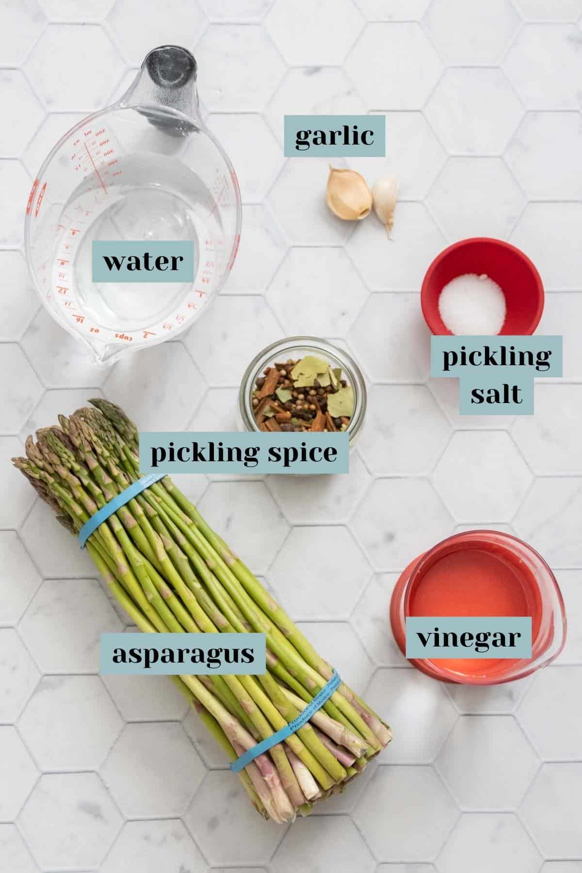 Ingredients for pickled asparagus on a tile surface with labels.