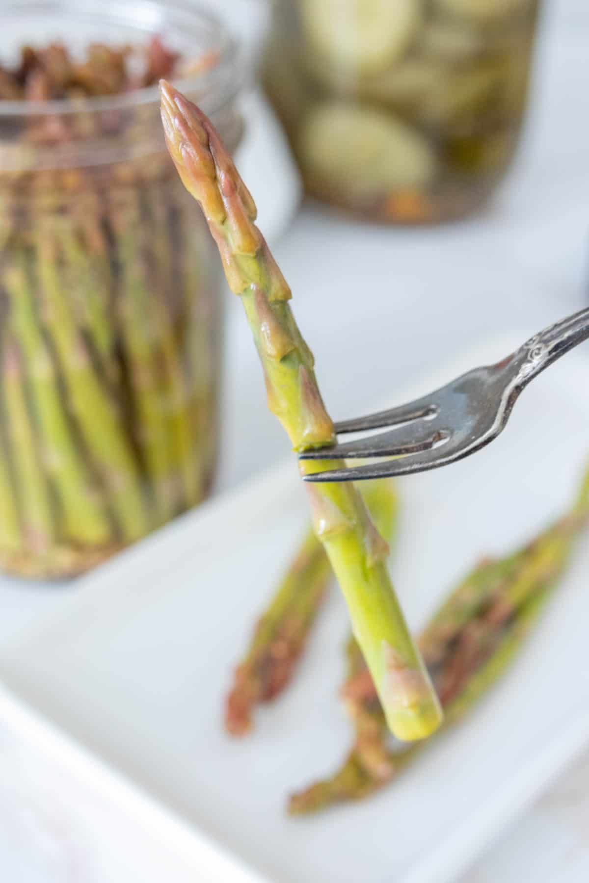 Pickle fork holding up a spear of pickled asparagus.