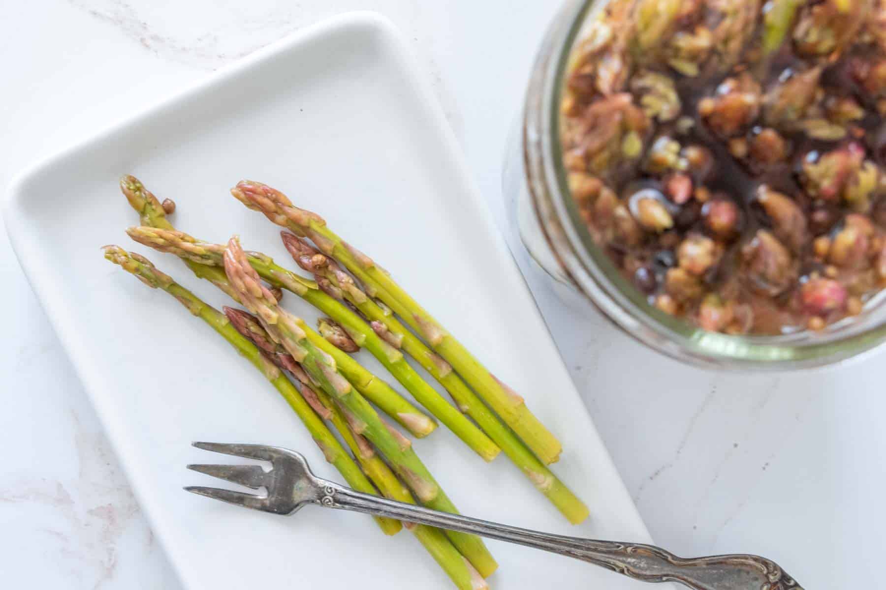 Pickled asparagus on a plate with a pickle fork on top.