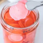 Tongs holding up two slices of pickled radish.