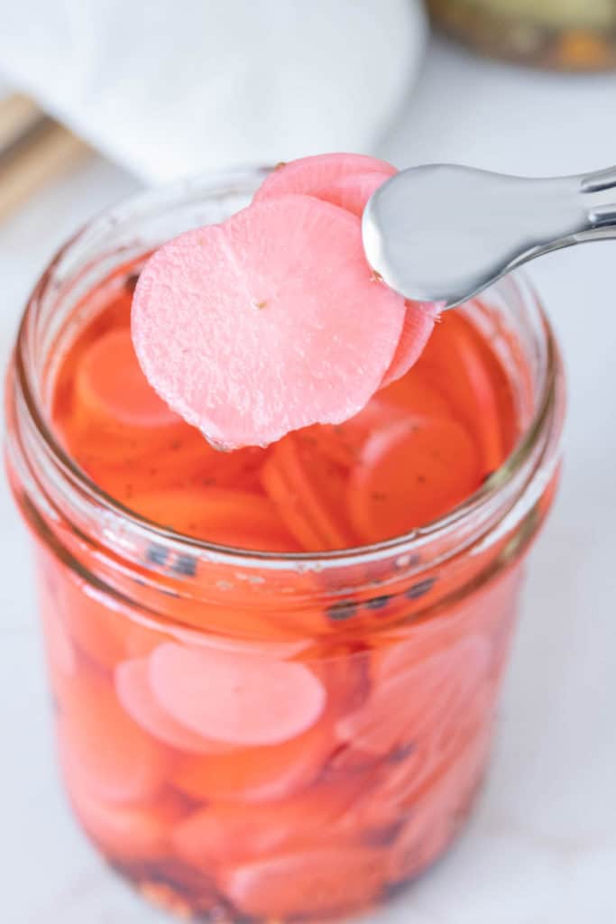 Tongs holding up two slices of pickled radish.