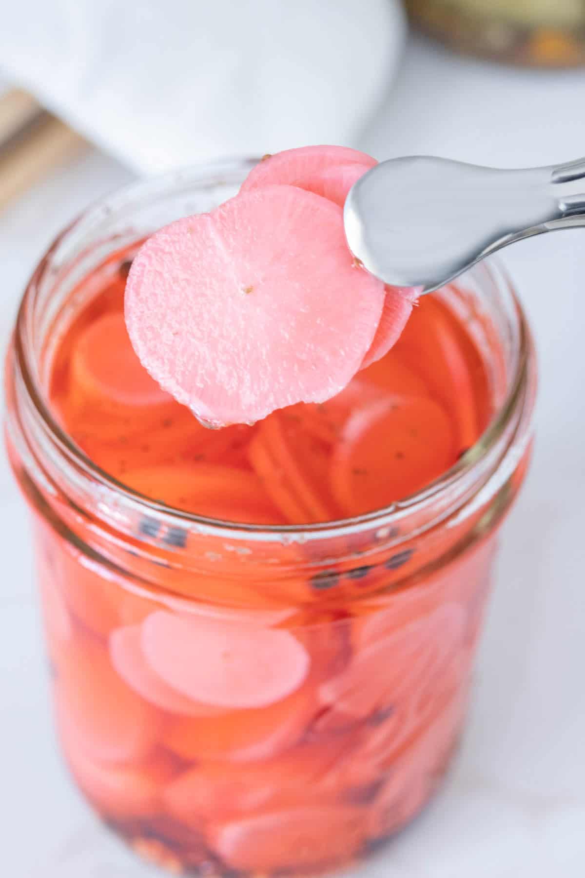 Tongs holding up two slices of pickled radish.