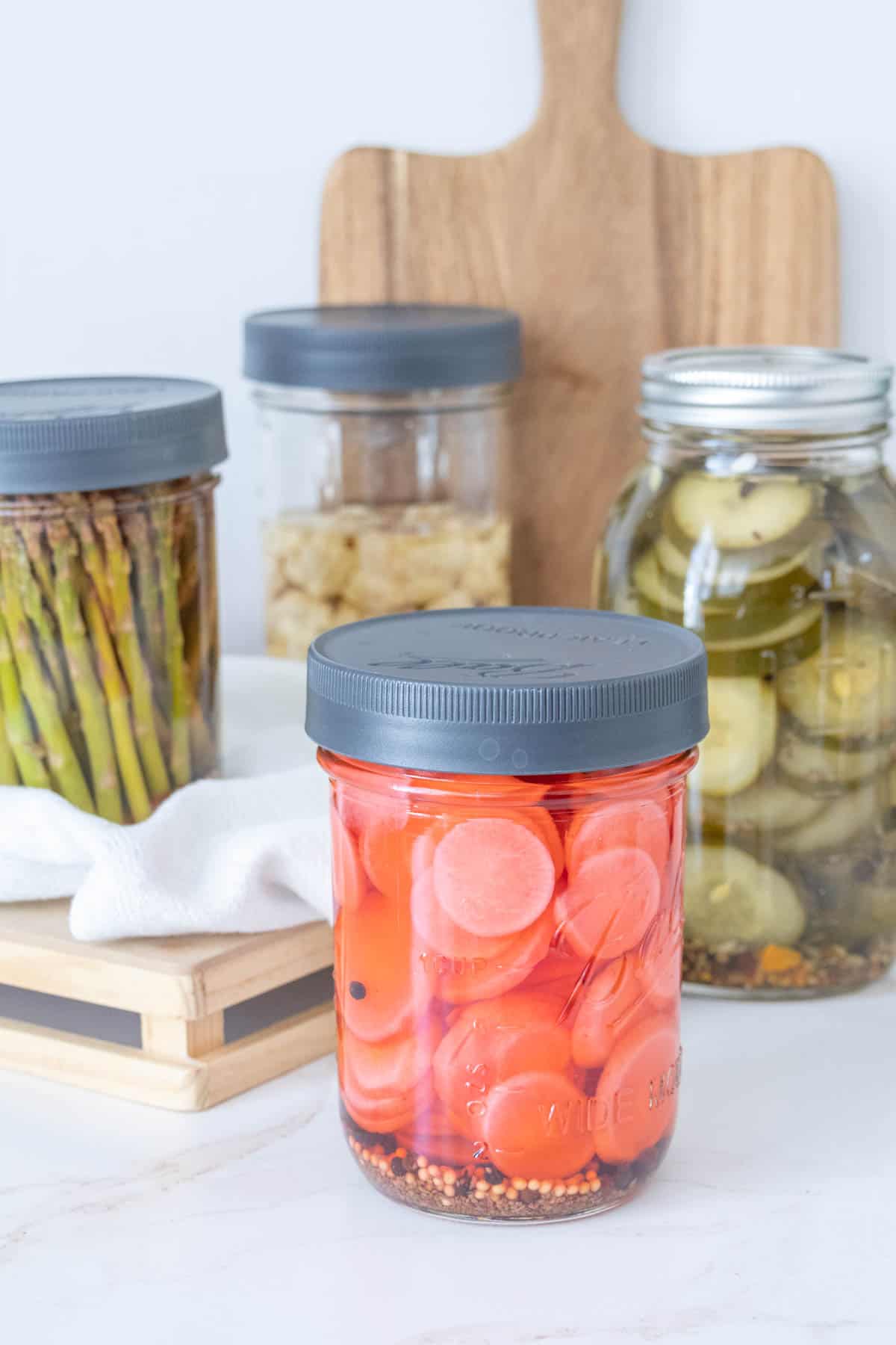 Jars of pickles with pickled radishes in front.