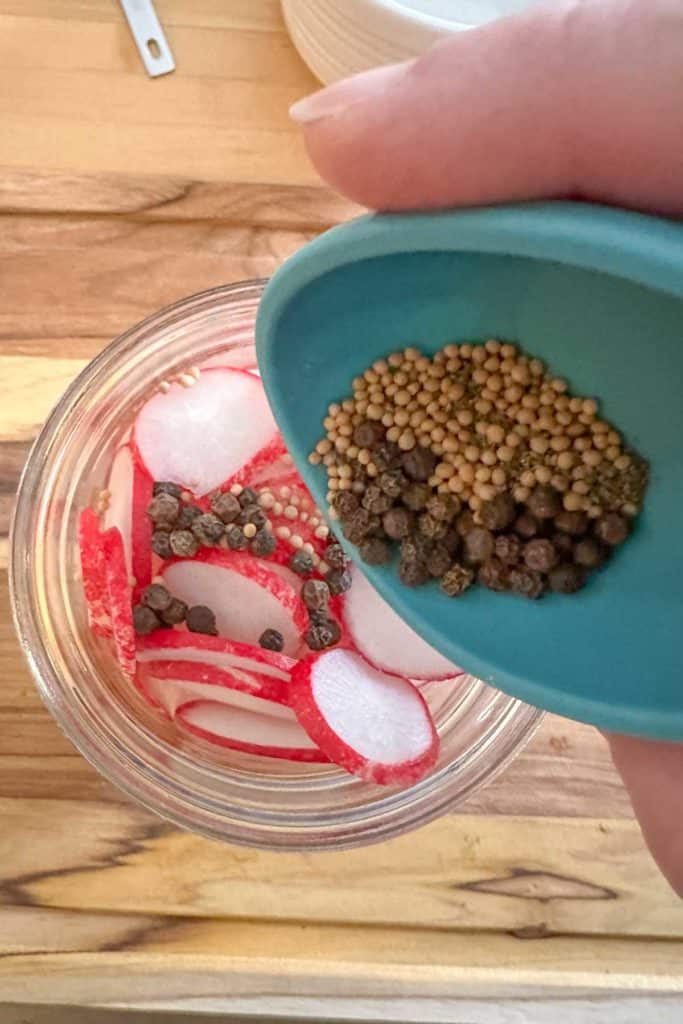 Pouring spices into a jar of sliced radishes.