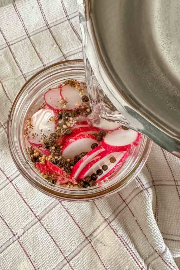 Pouring brine into jar of radishes and spices.