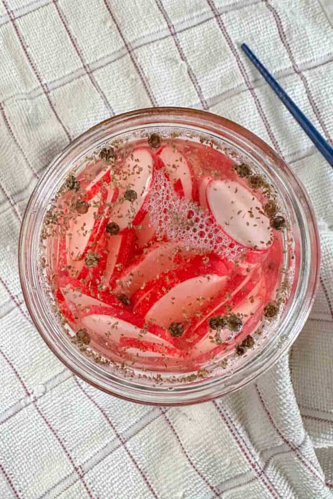 Jar of radishes in pickling brine sitting on a towel from overhead.