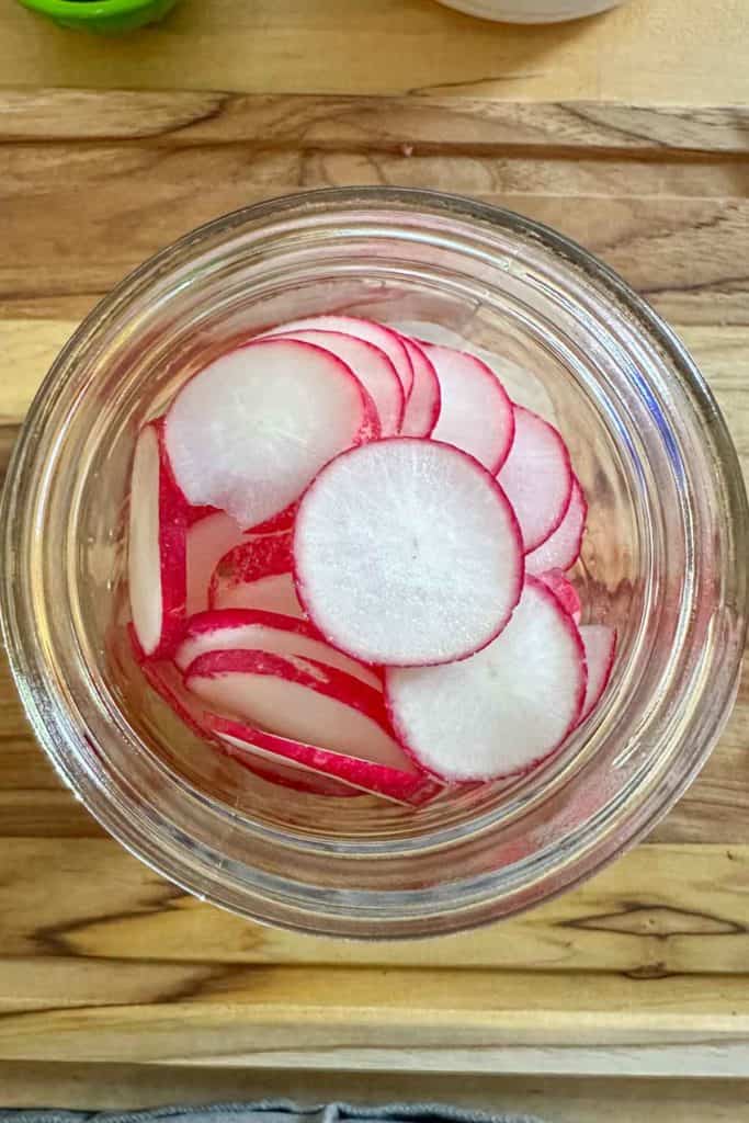 Glass jar filled with sliced radishes shot from overhead.