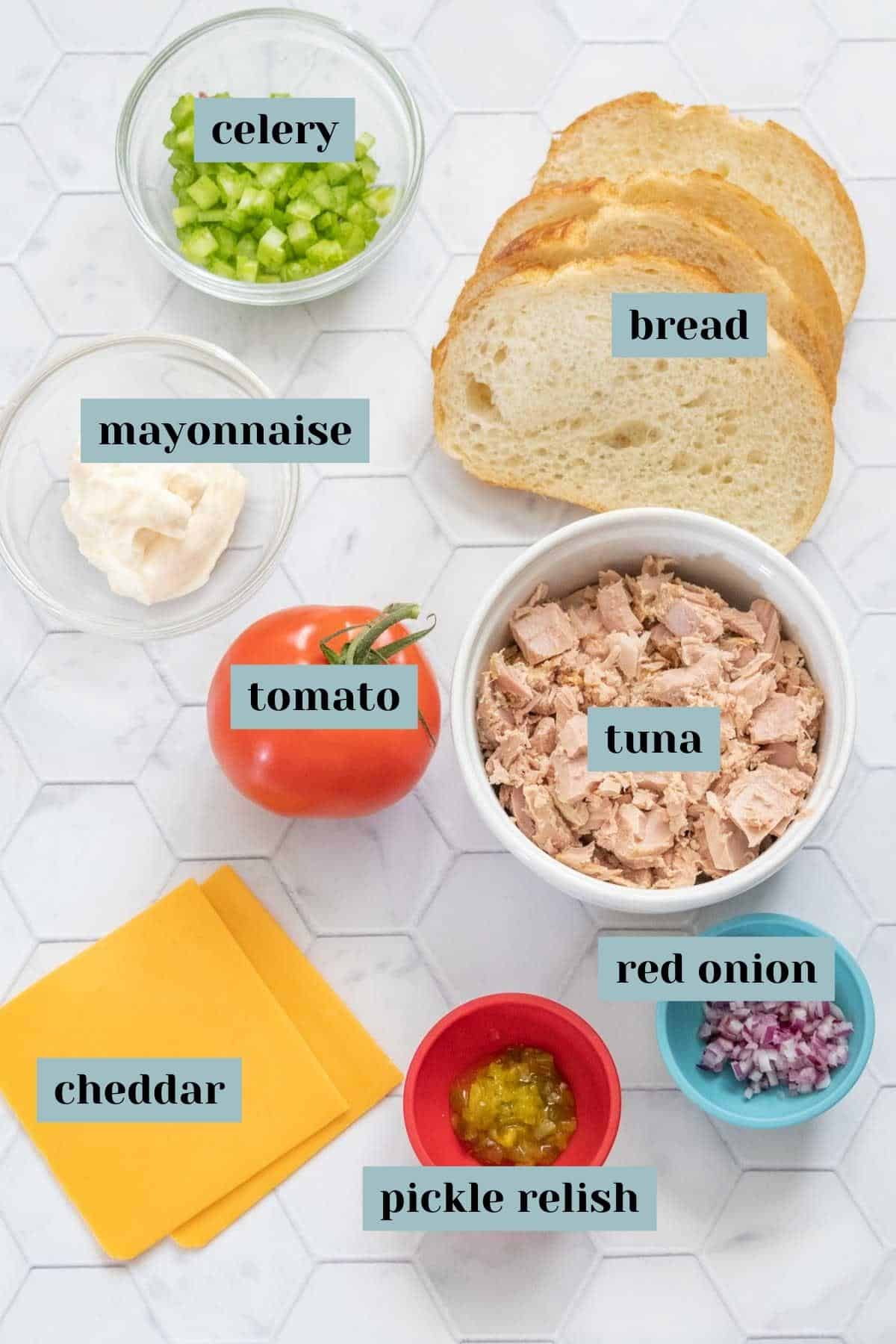 Ingredients for tuna melt sandwich on tile surface with labels.