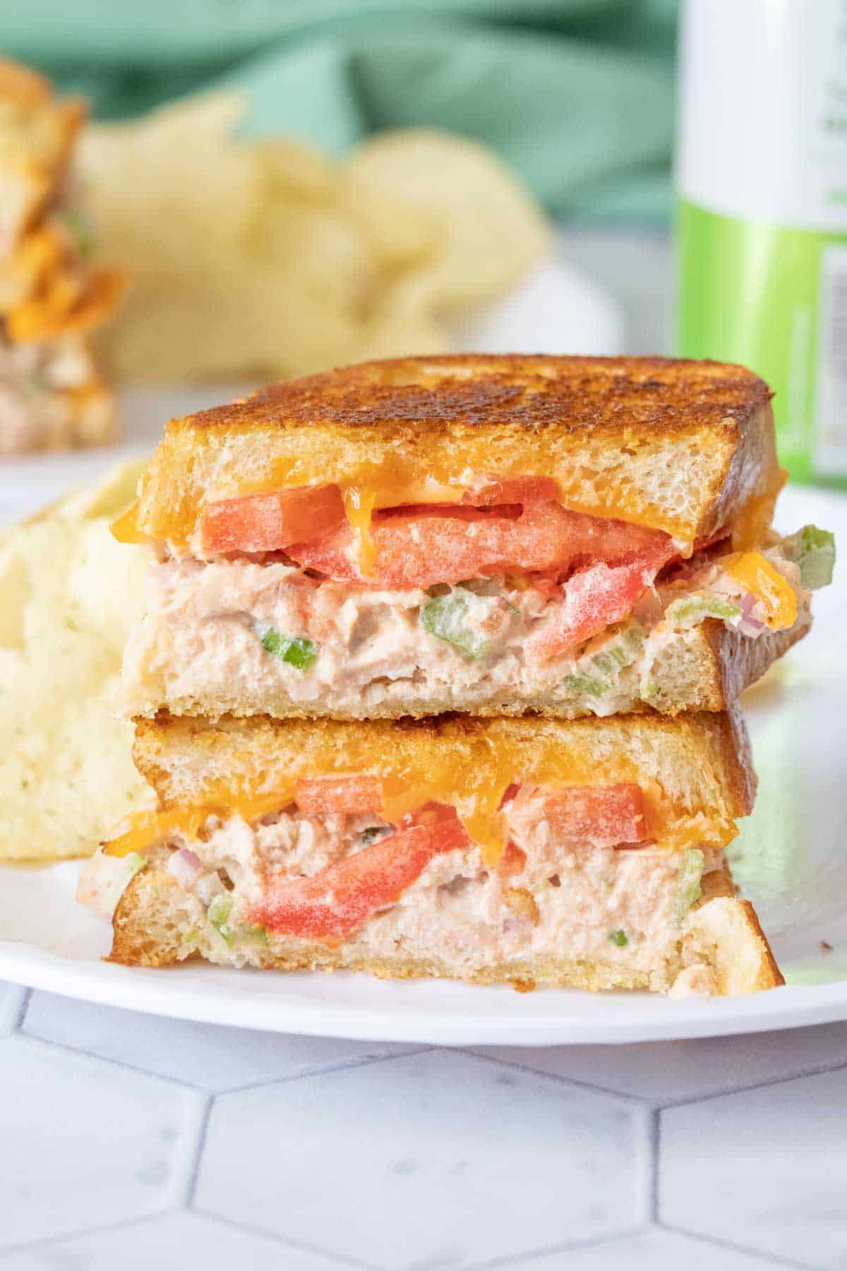 Two halves of a tuna melt stacked on a white plate, cut to show interior of sandwich.