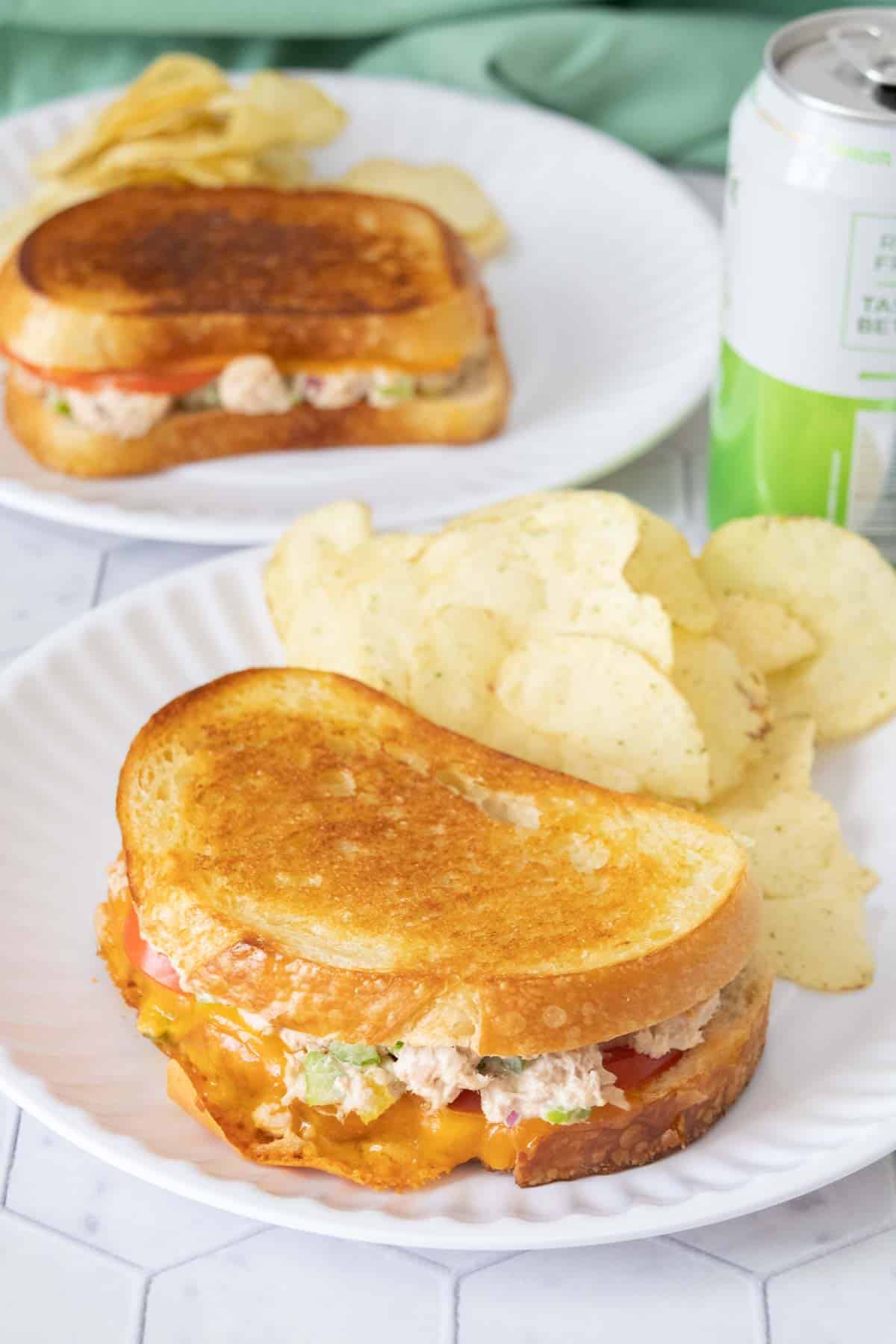 Tuna melt sandwich on white plate with potato chips beside.