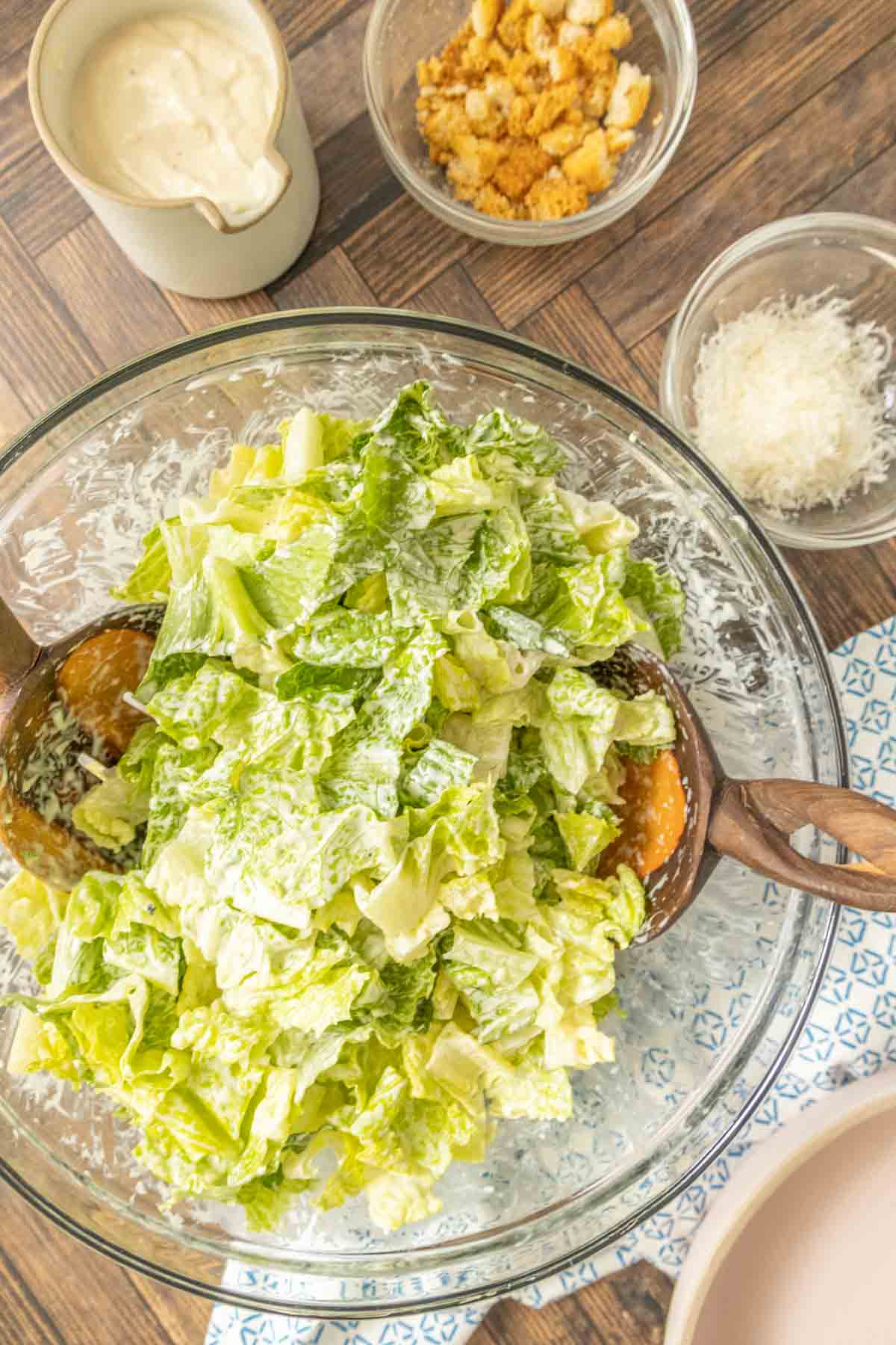 Romaine lettuce in a glass mixing bowl being tossed with Caesar dressing.