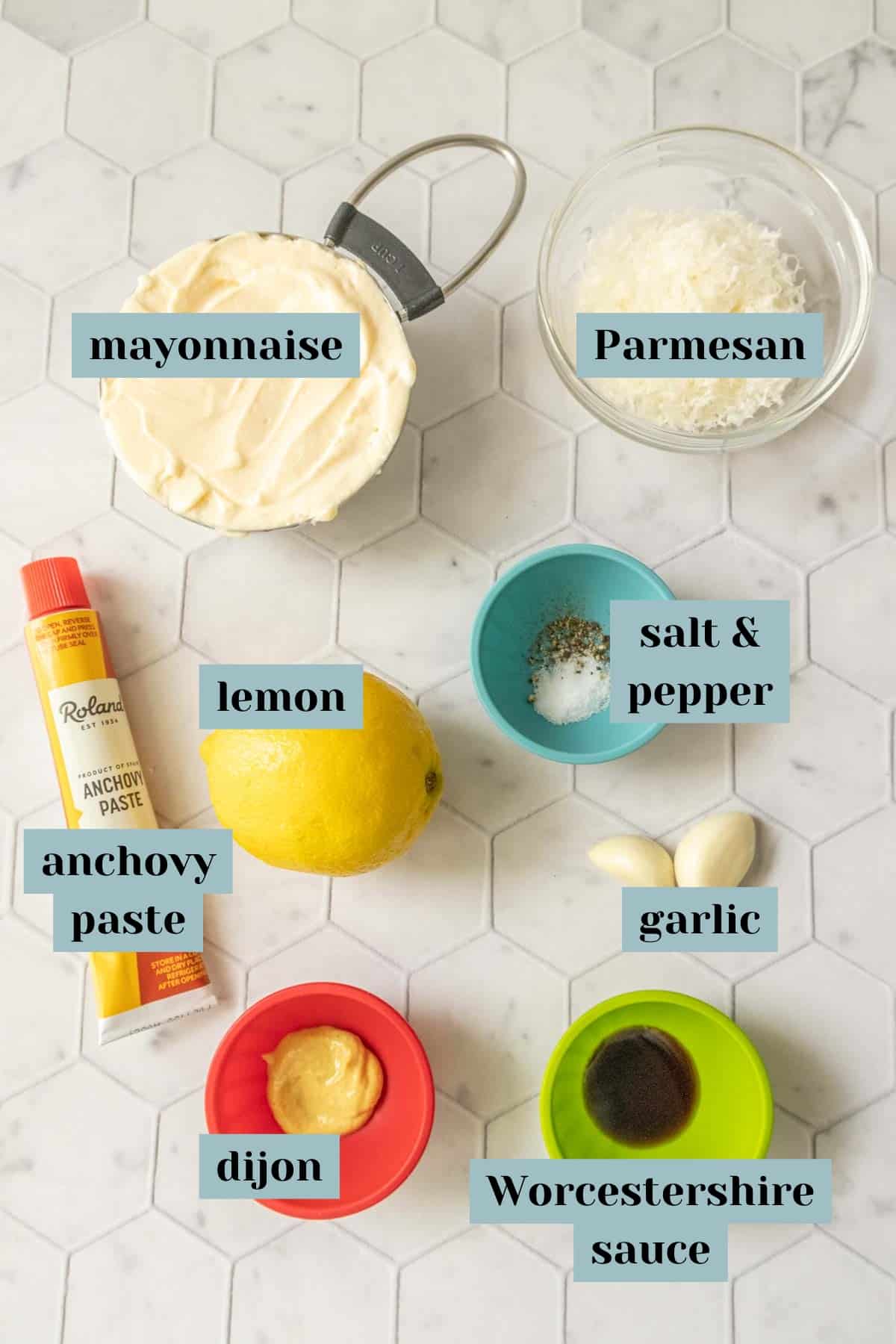 Ingredients for Caesar salad dressing on a tile surface with labels.