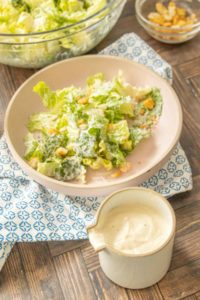 Caesar salad dressing in a ceramic cruet with a Caesar salad behind.