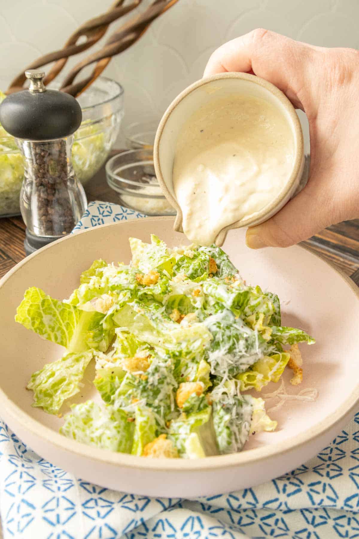 Pouring Caesar salad dressing onto a Caesar salad.