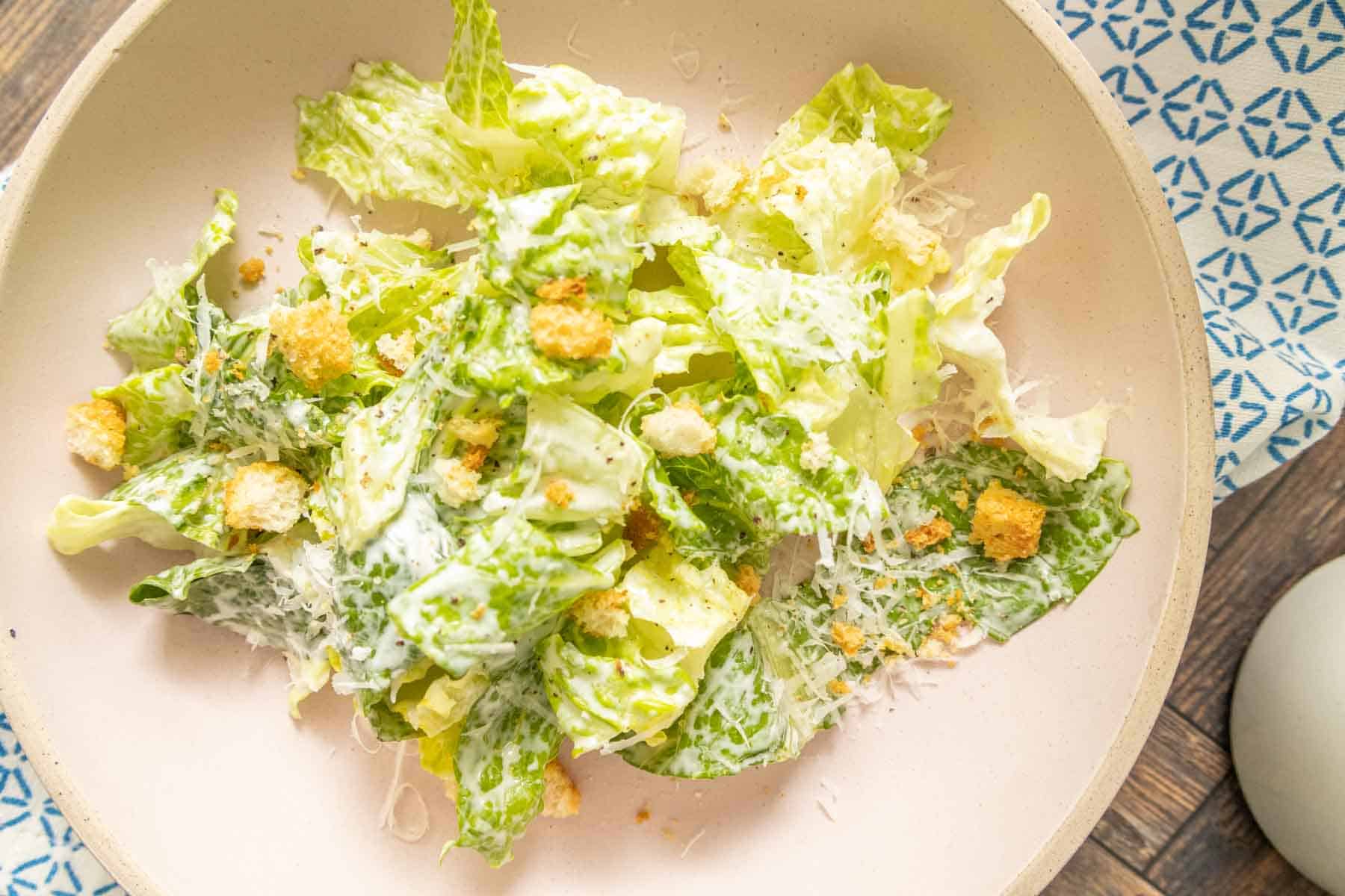 Overhead of a dressed Caesar salad on a pink plate.