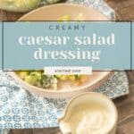 A bowl of Caesar salad sits next to a small pitcher of creamy Caesar salad dressing on a wooden table with a blue patterned napkin.
