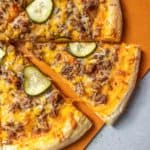 Cheeseburger pizza on a pizza peel with one slice being pulled away.