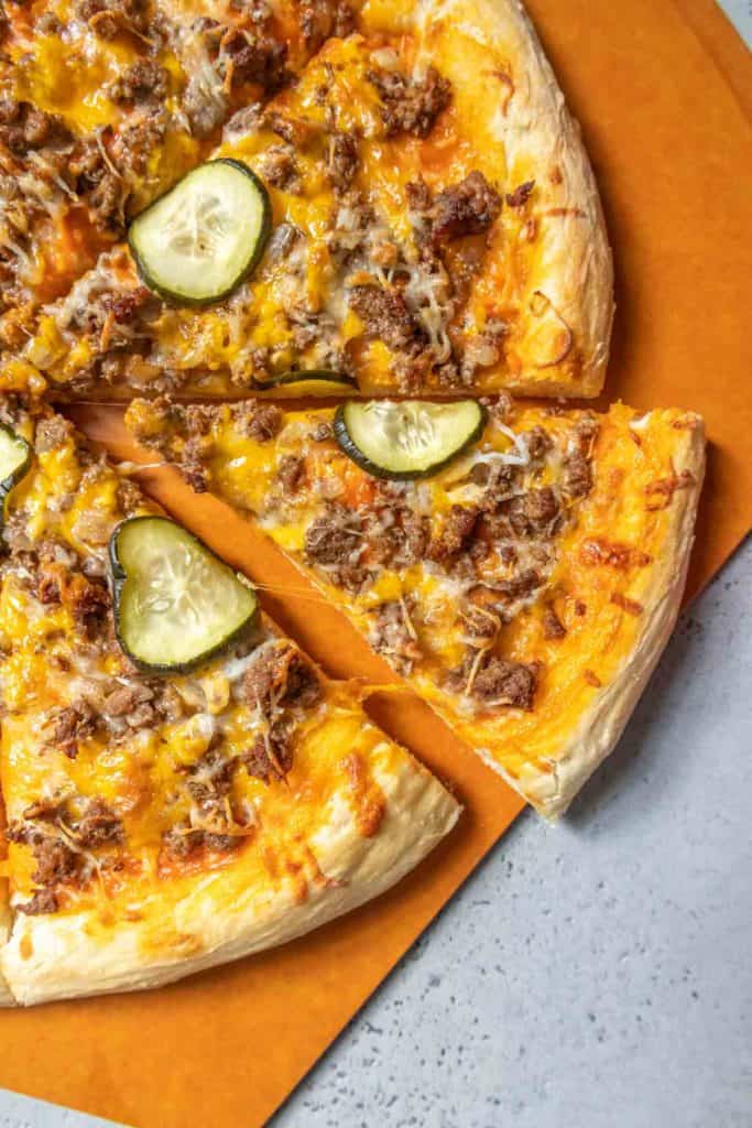Cheeseburger pizza on a pizza peel with one slice being pulled away.