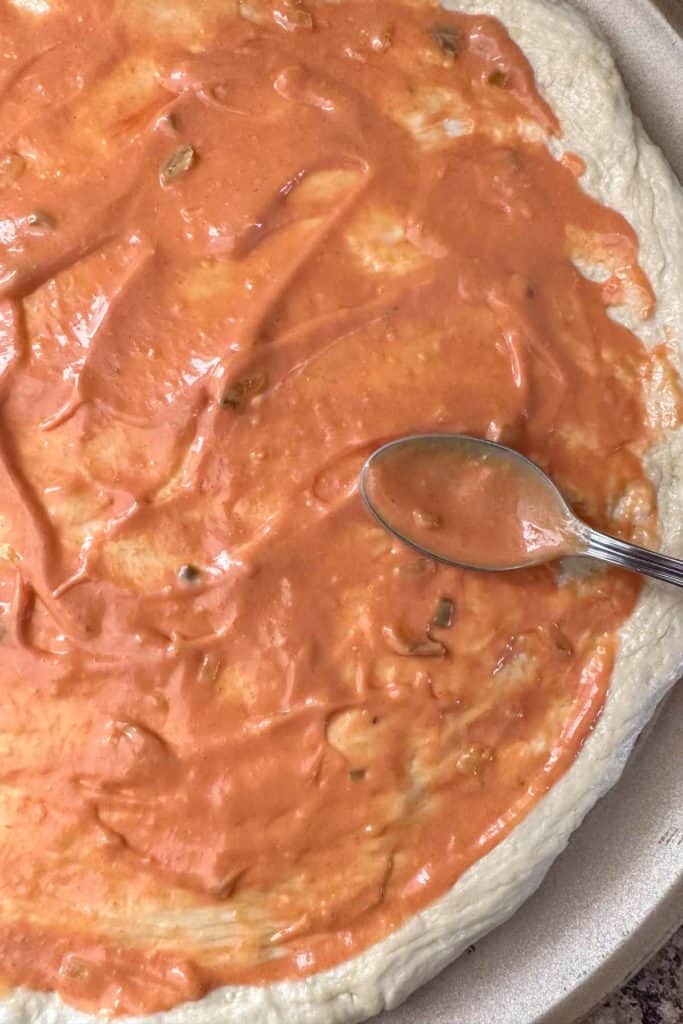 Spreading homemade burger sauce onto unbaked pizza dough.