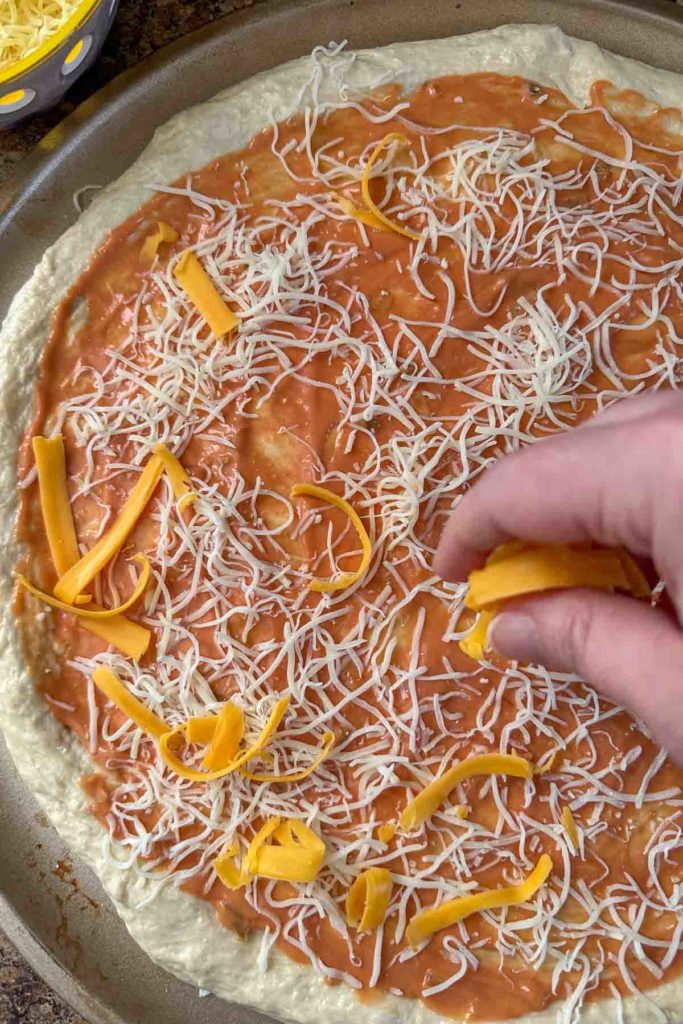 Sprinkling cheese onto unbaked pizza crust.
