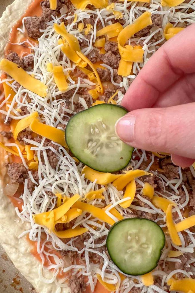 Adding pickles to cheeseburger pizza.