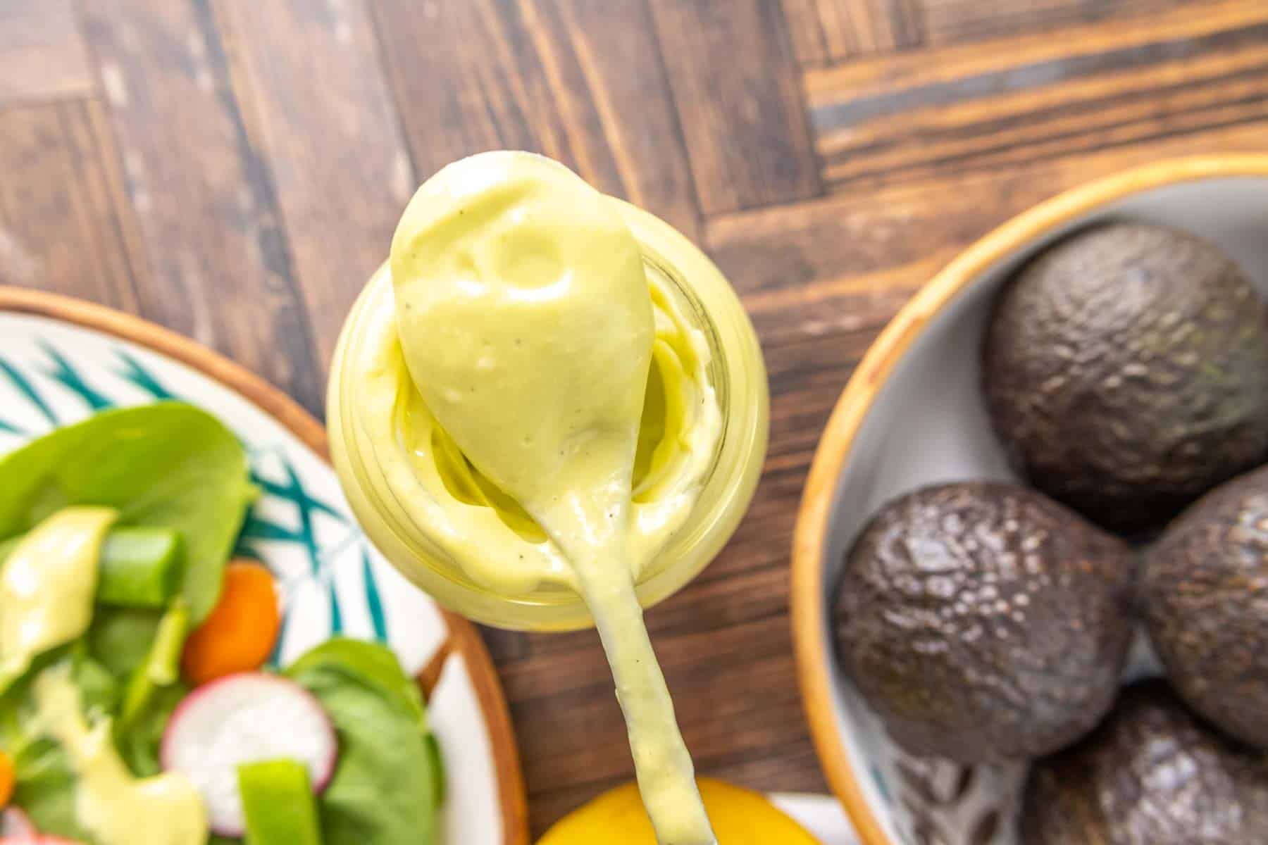 Spoonful of avocado dressing sitting on bottle, with avocados and salad on either side.