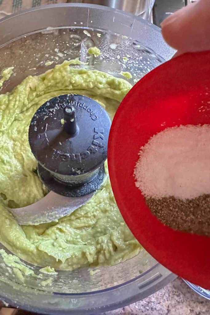 Adding salt and pepper to blended avocado in a food processor.