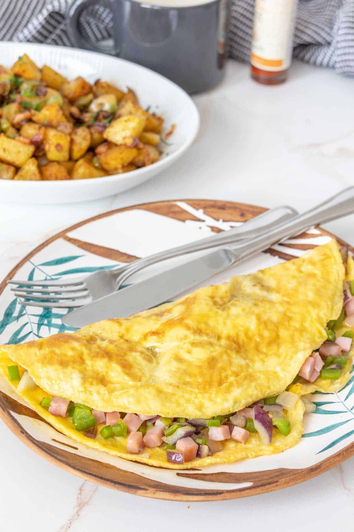 Denver omelet on a plate with a plate of breakfast potatoes behind.